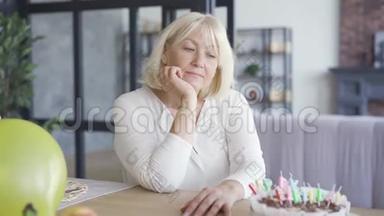 悲伤不快乐的成熟女人坐在桌子前的小<strong>生日</strong>蛋糕在埃姆比房间。 <strong>生日庆典</strong>